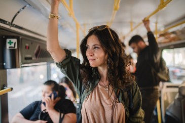 Woman riding bus, standing, holding on to safety bar