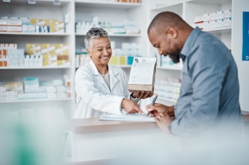 Man at pharmacy counter with pharmacist, smiling