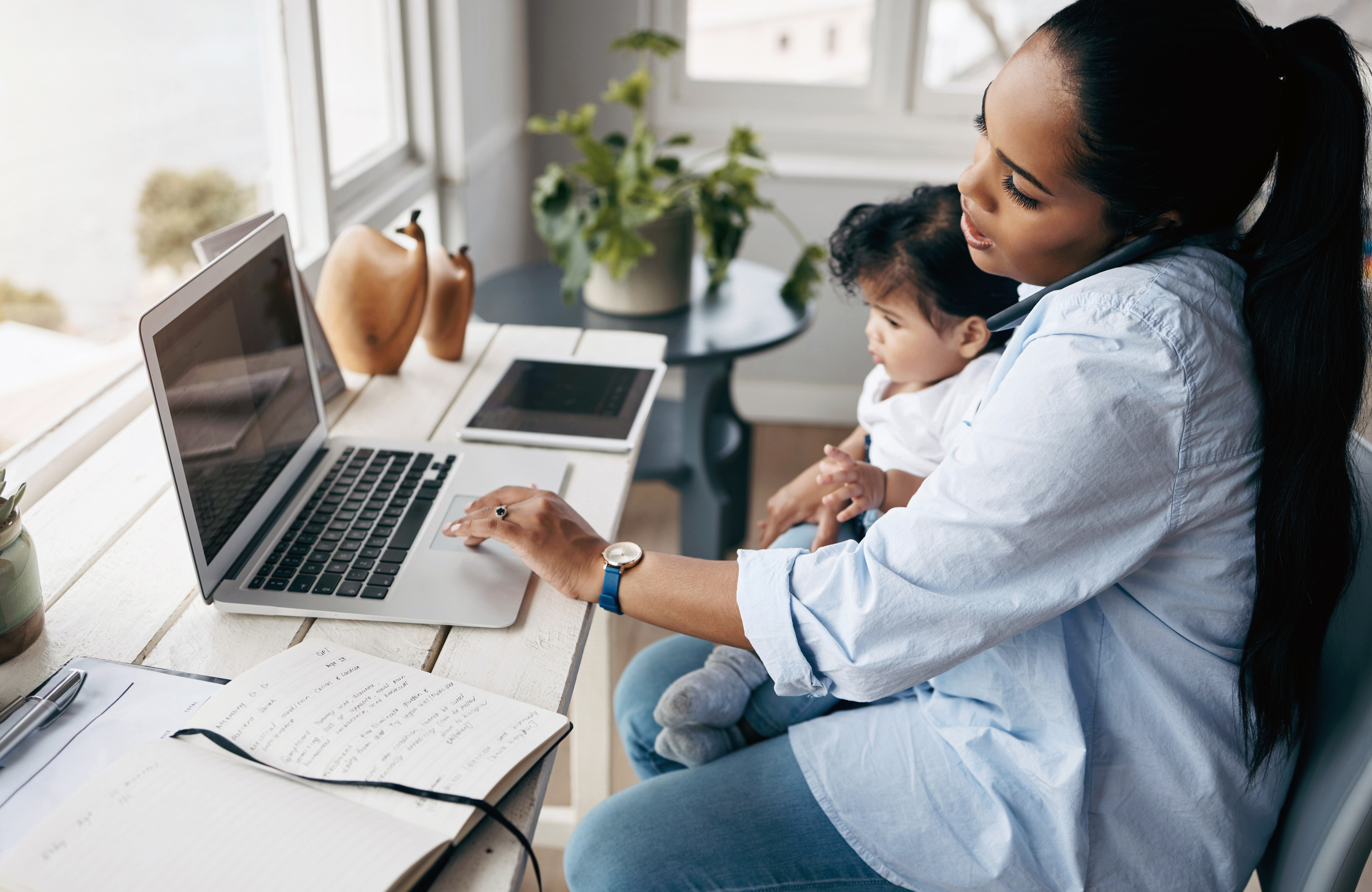Mom holding child in lap while on phone and working at computer