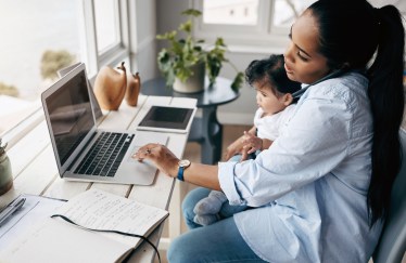 Mom holding child in lap while on phone and working at computer