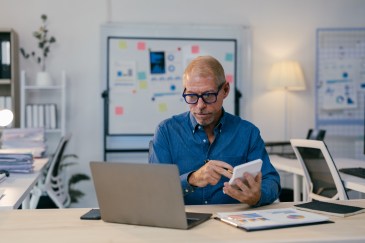Man holding a calculator while looking at his computer