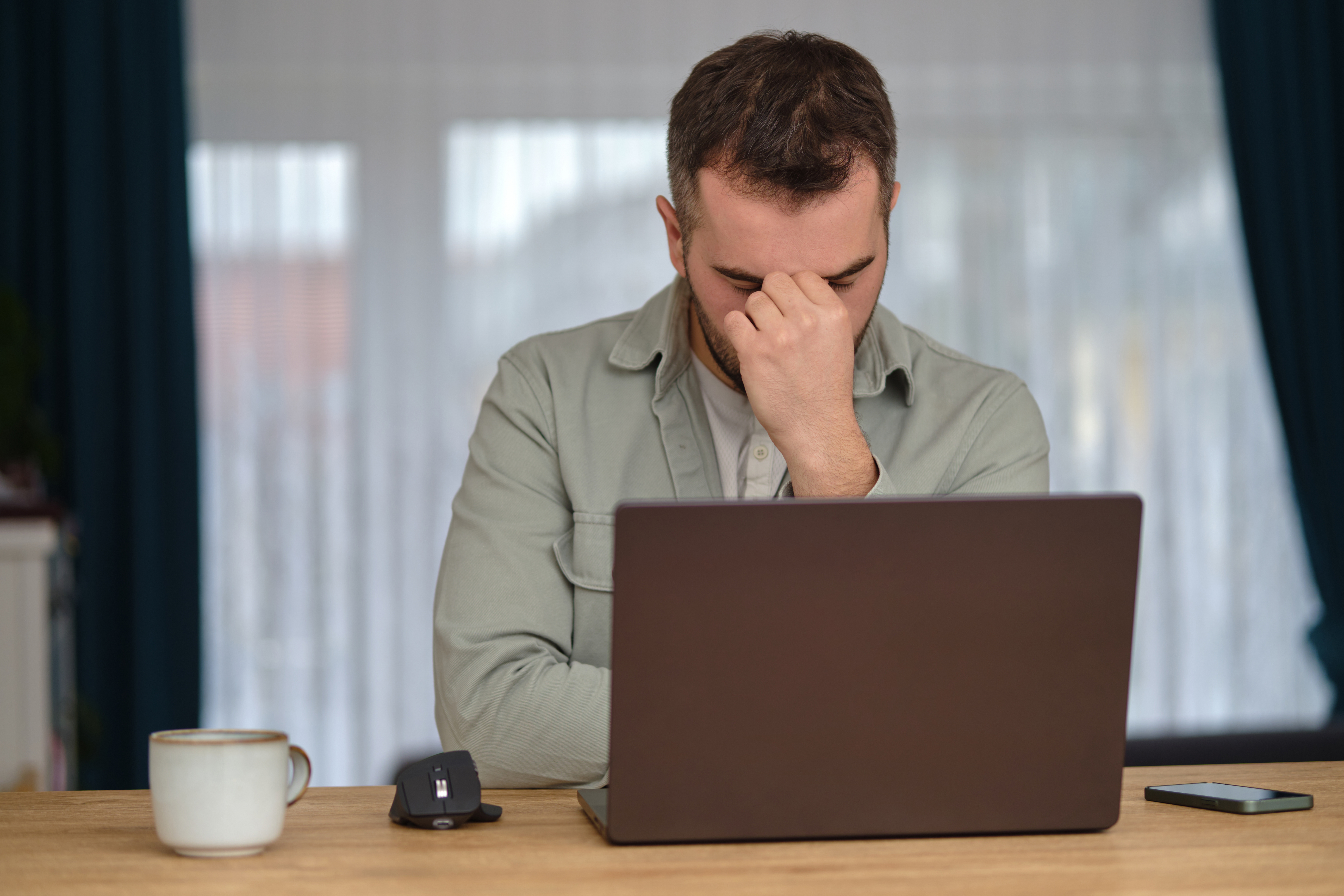 Man with hand on face, sitting in front of computer, distressed, tired
