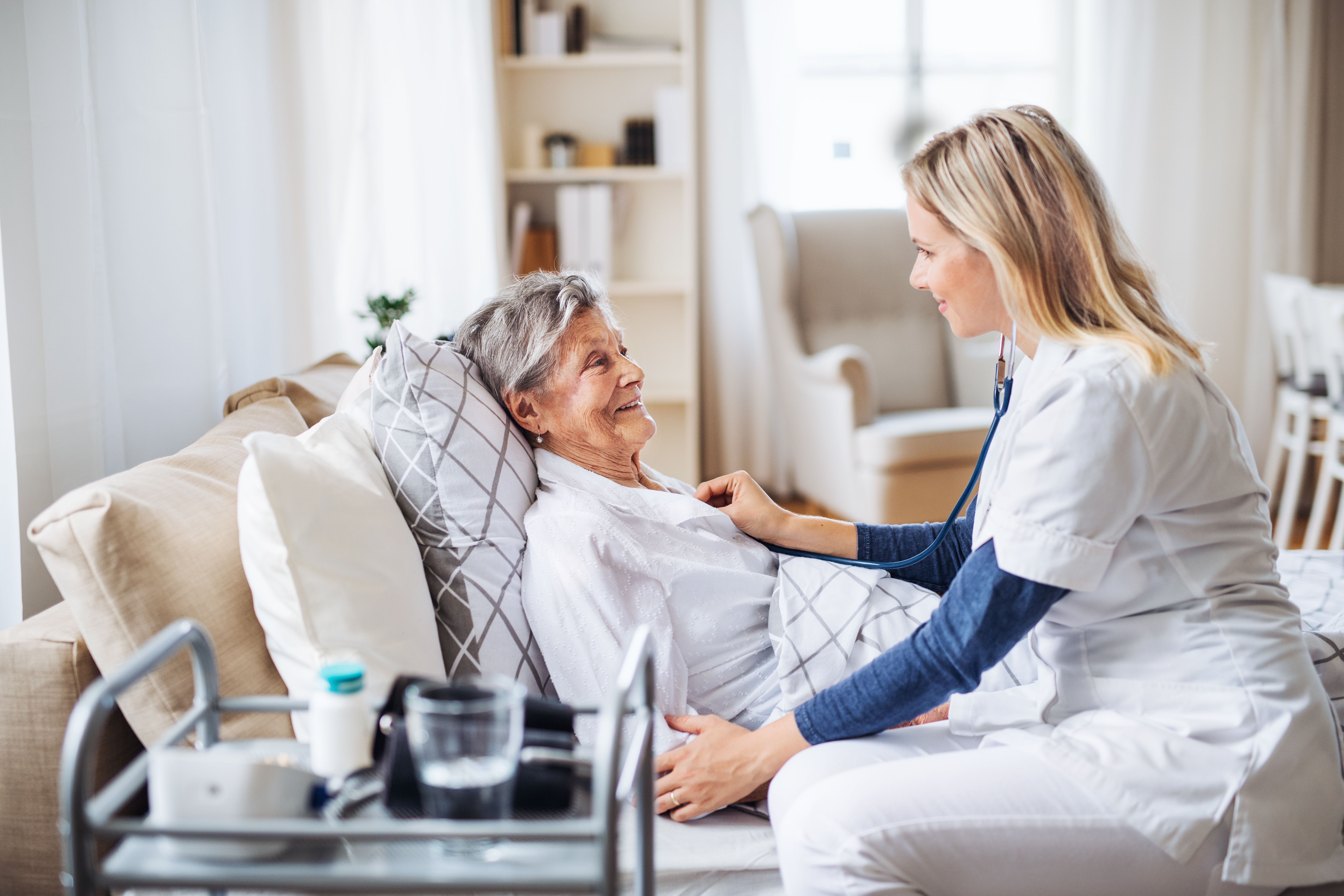 Nurse checking heartbeat of older patient laying on couch in home