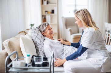 Nurse checking heartbeat of older patient laying on couch in home