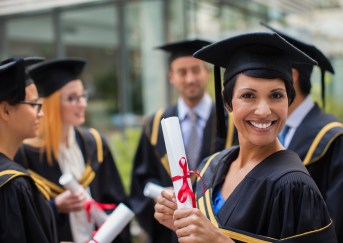 Adult woman in gap and gown, holding diploma and smiling, graduating from college