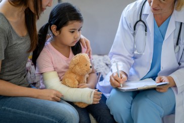 Mom sitting with daughter whose arm is in cast, next to doctor writing
