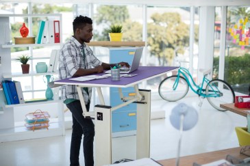 Man working at standing desk, bright colors, bicycle inside