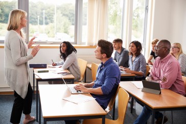Adults sitting in classroom, instructor standing in front, speaking