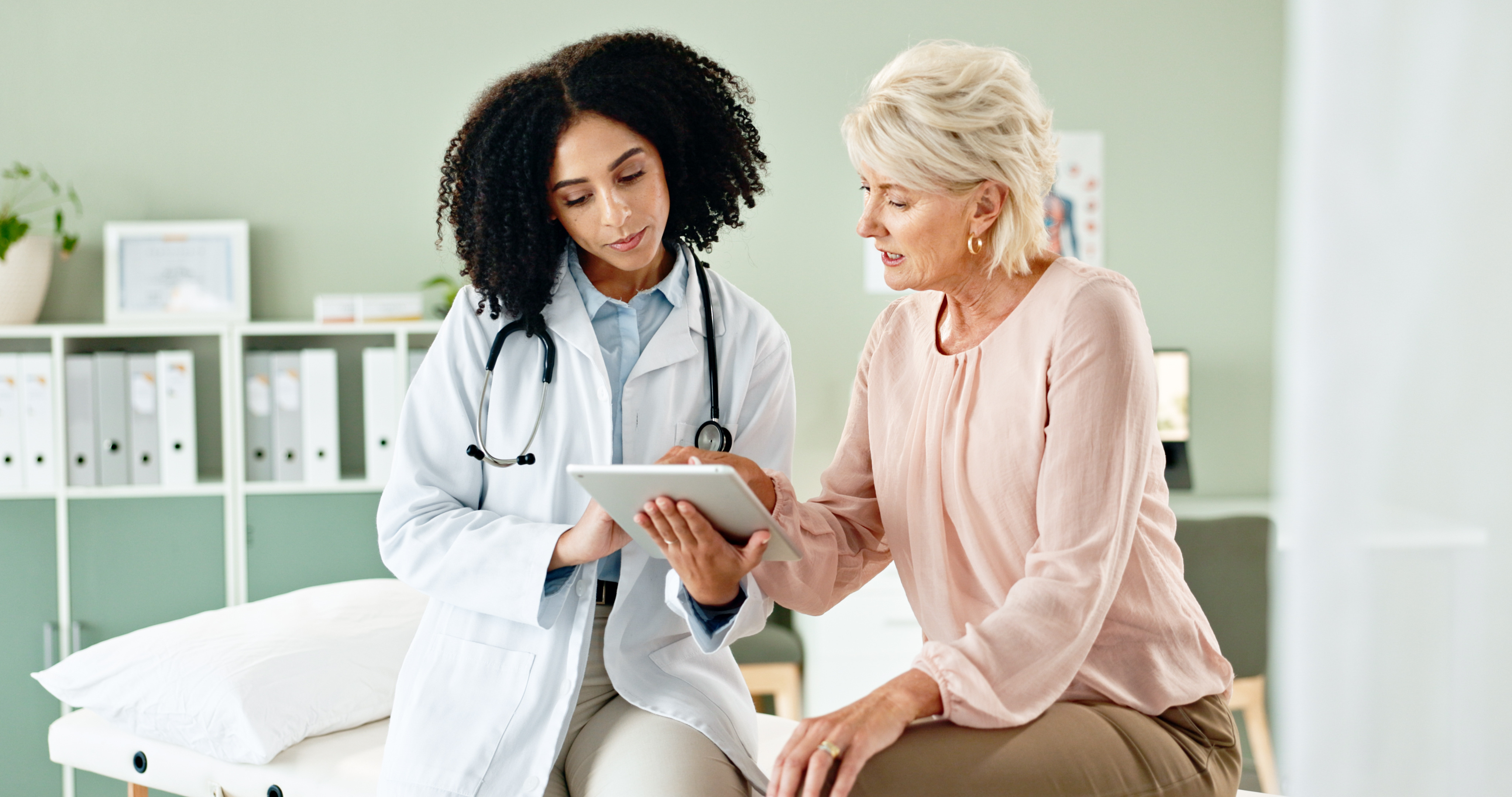 Woman speaking with female doctor, looking at tablet in doctor's office