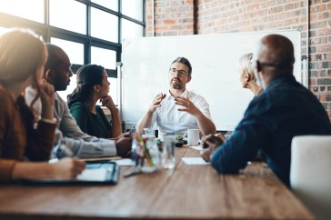 Man sitting at head of conference table, talking with other employees