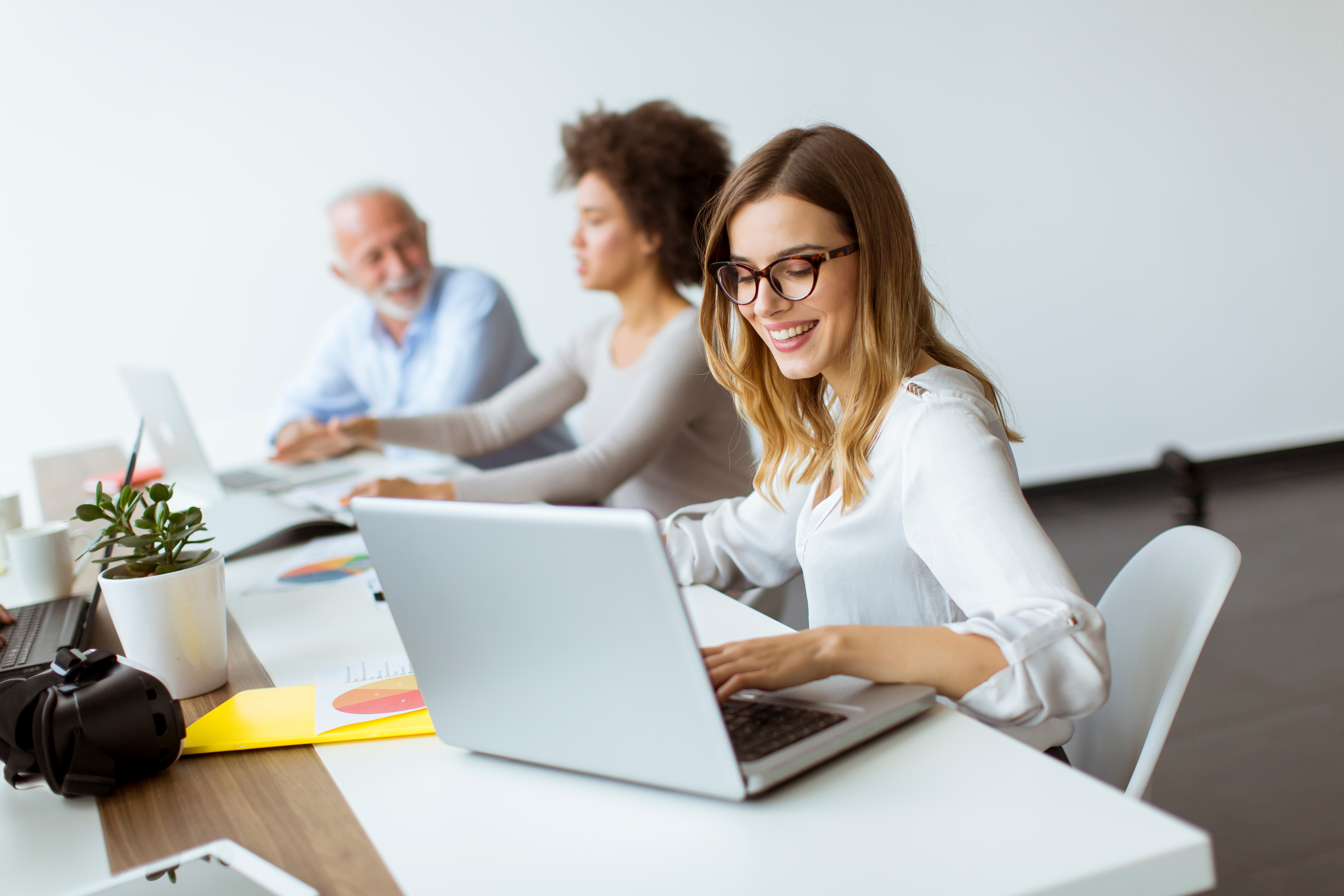 People working at long desk, female employee working on laptop, smiling