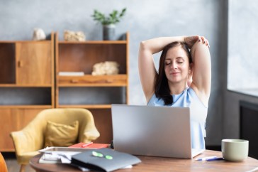 Woman stretching at home, using laptop