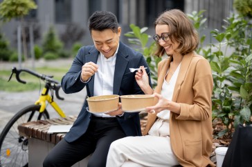 Two employees sitting outside, eating, smiling