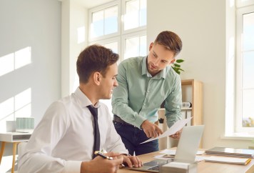 Two male coworkers looking at paper, one explaining