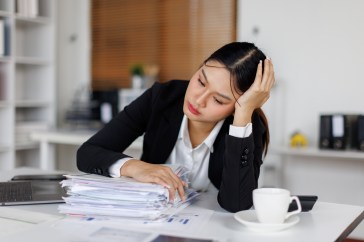 Woman at work leaning on desk, head in hand, looking stressed