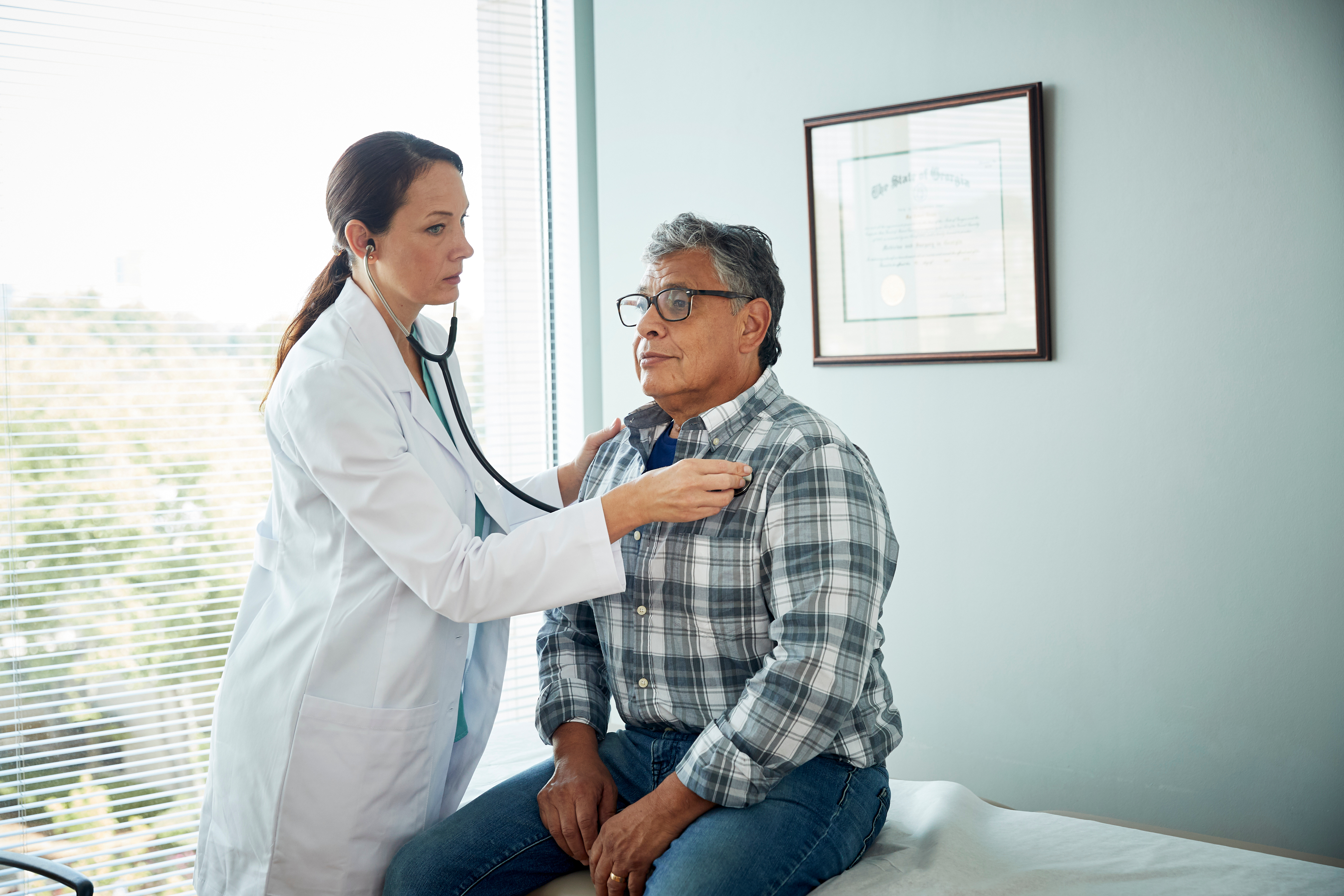 Man sitting on exam table, getting heart examined by doctor
