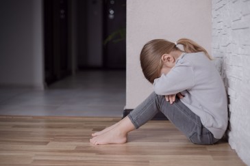 Little girl leaning against wall with head in arms