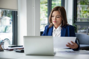 Woman looking at paper and computer sitting at desk