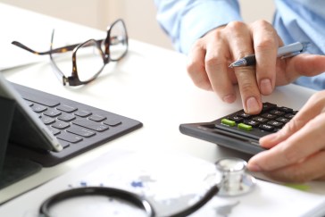 A man using a calculator sitting in front of a laptop.