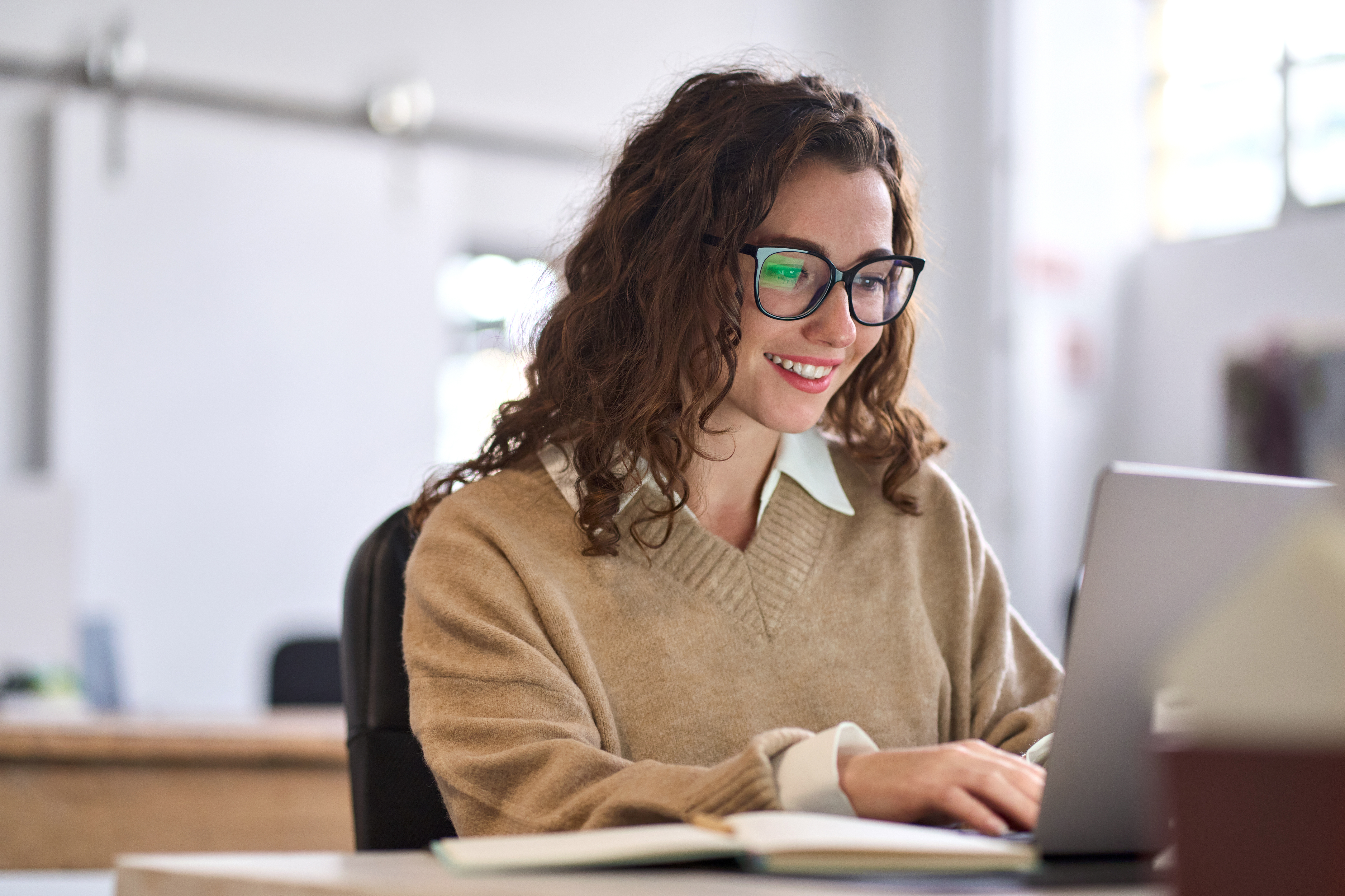 Woman sitting at desk, smiling, working on laptop