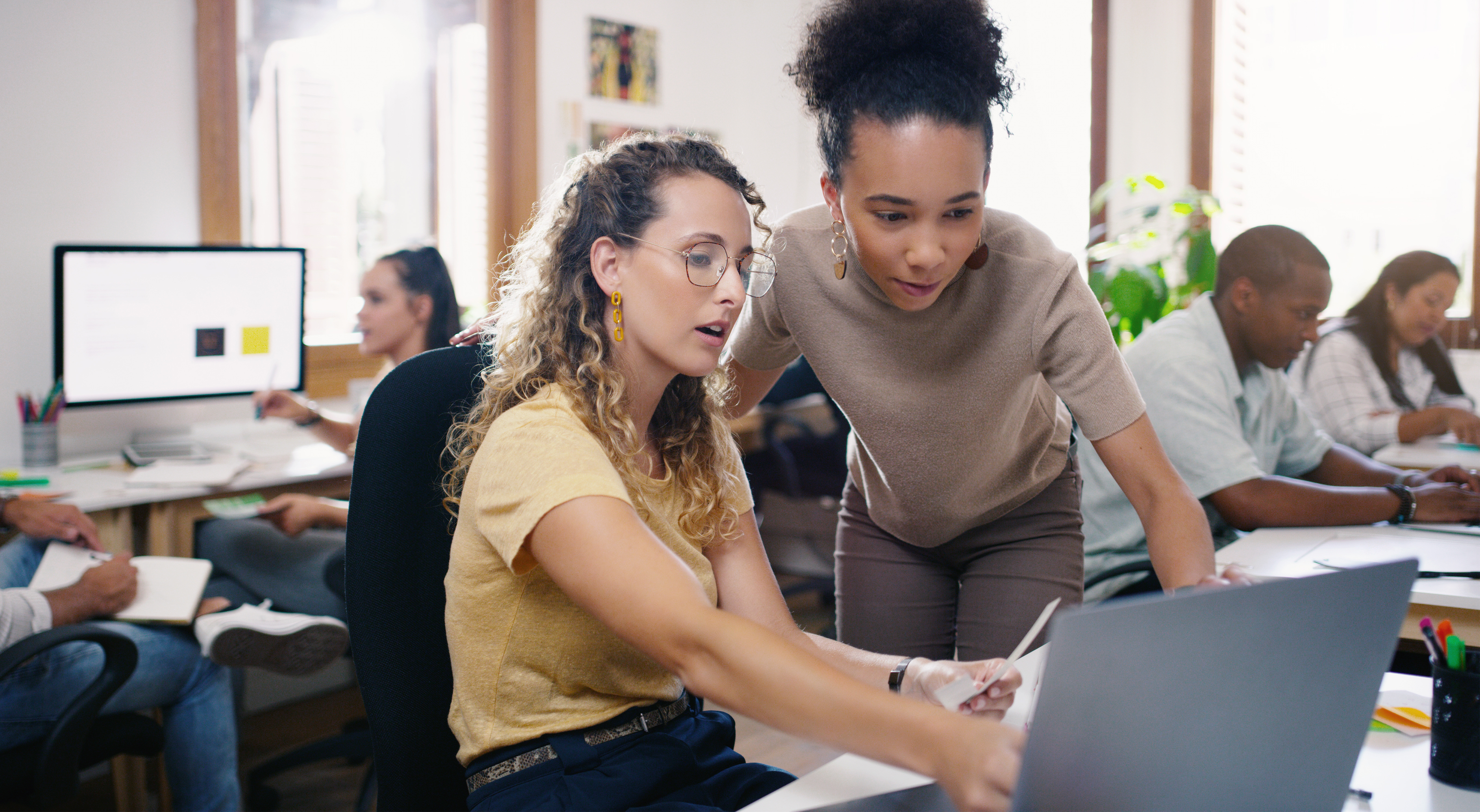 Two young female employees working in office, looking at computer