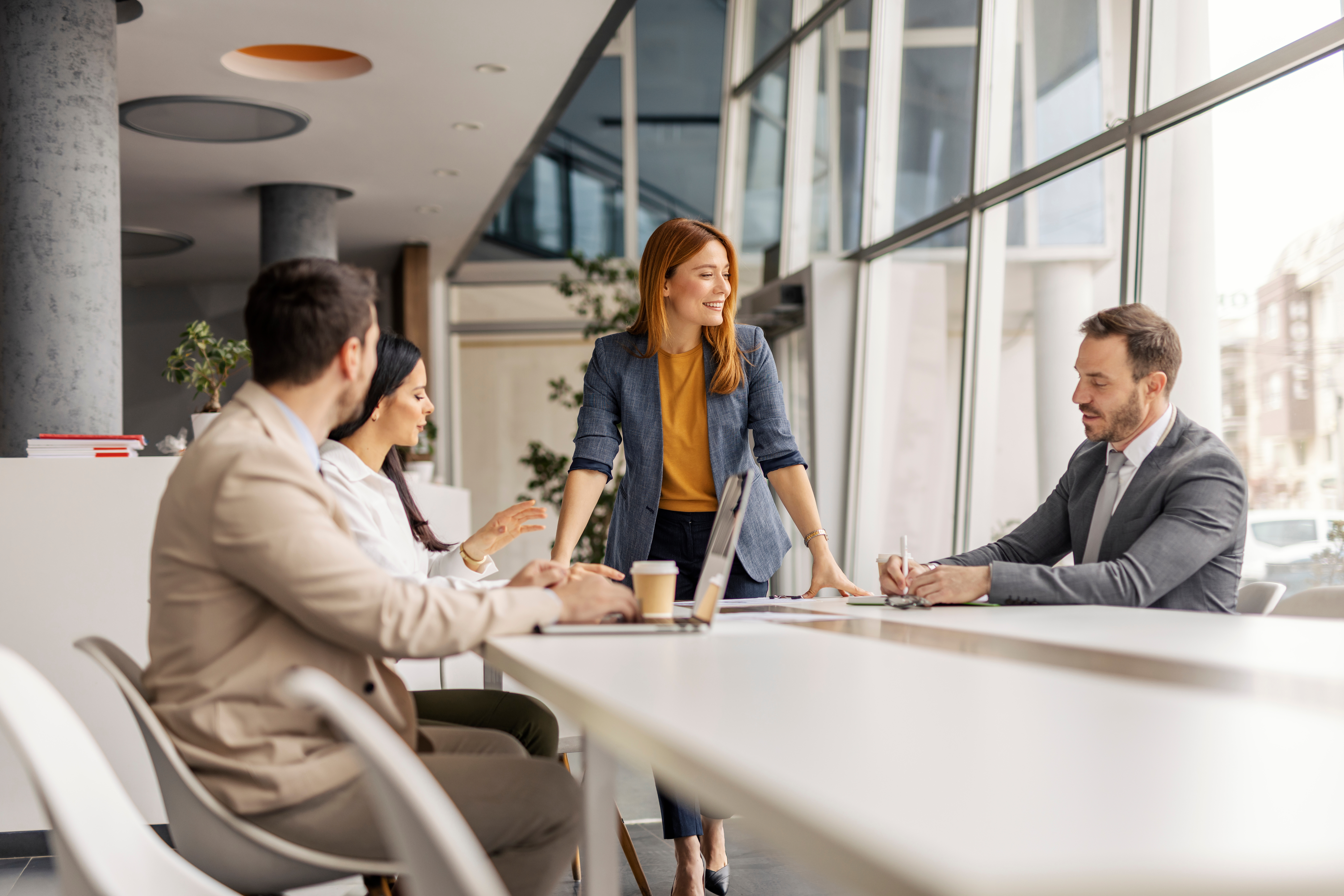 Woman standing at table, smiling, speaking to seated employees
