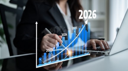 A person works on a laptop and points a pen at a bar chart.