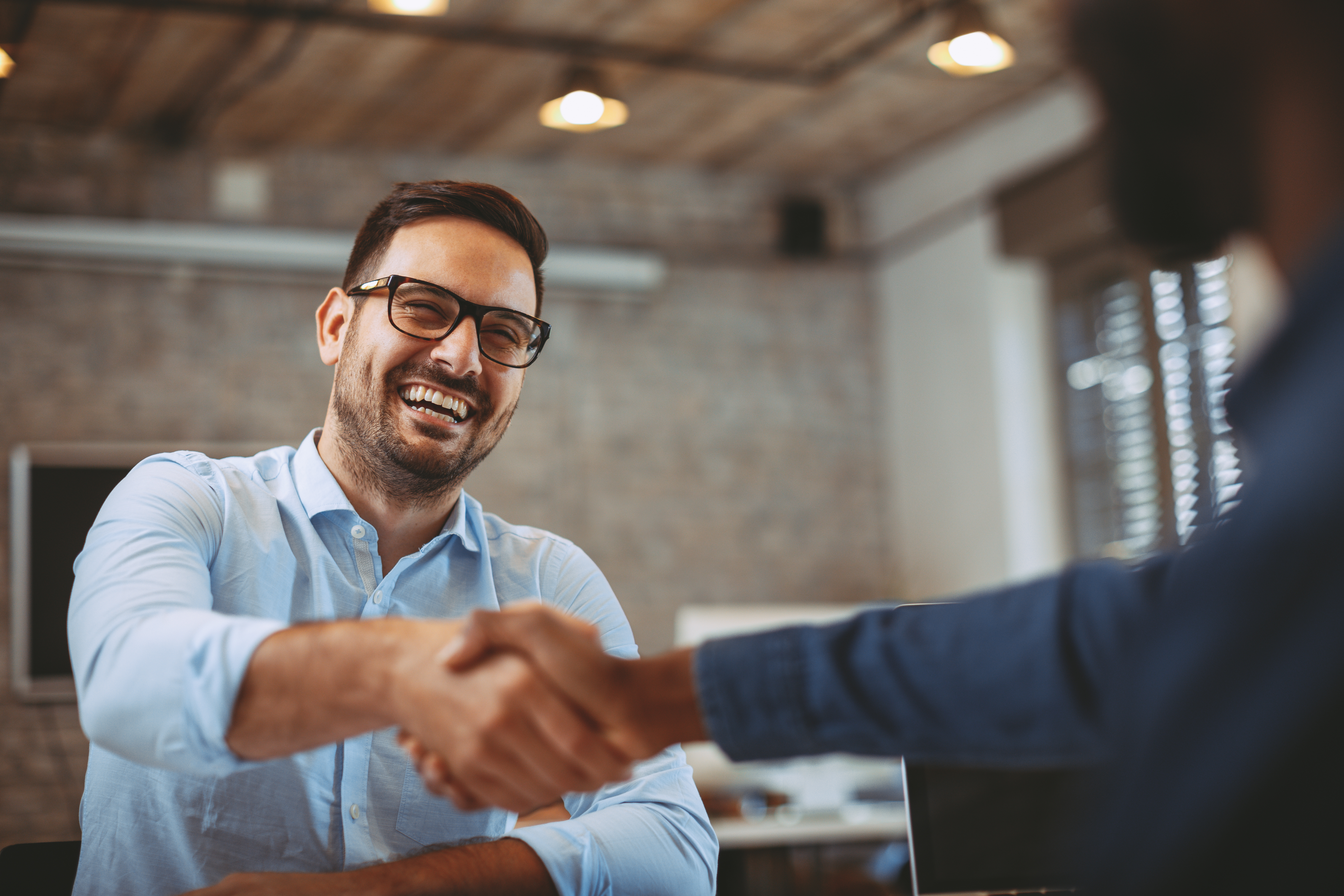 Man with glasses smiling, shaking hand, accepting job