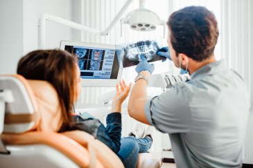 Woman in dentist chair, looking at X-rays with dentist
