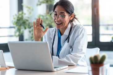 Female doctor greeting someone on computer, virtual meeting