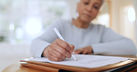 A woman holding a pen and writing on a sheet of paper.