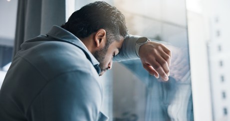 A man leans against a window with his head leaning against his forearm.