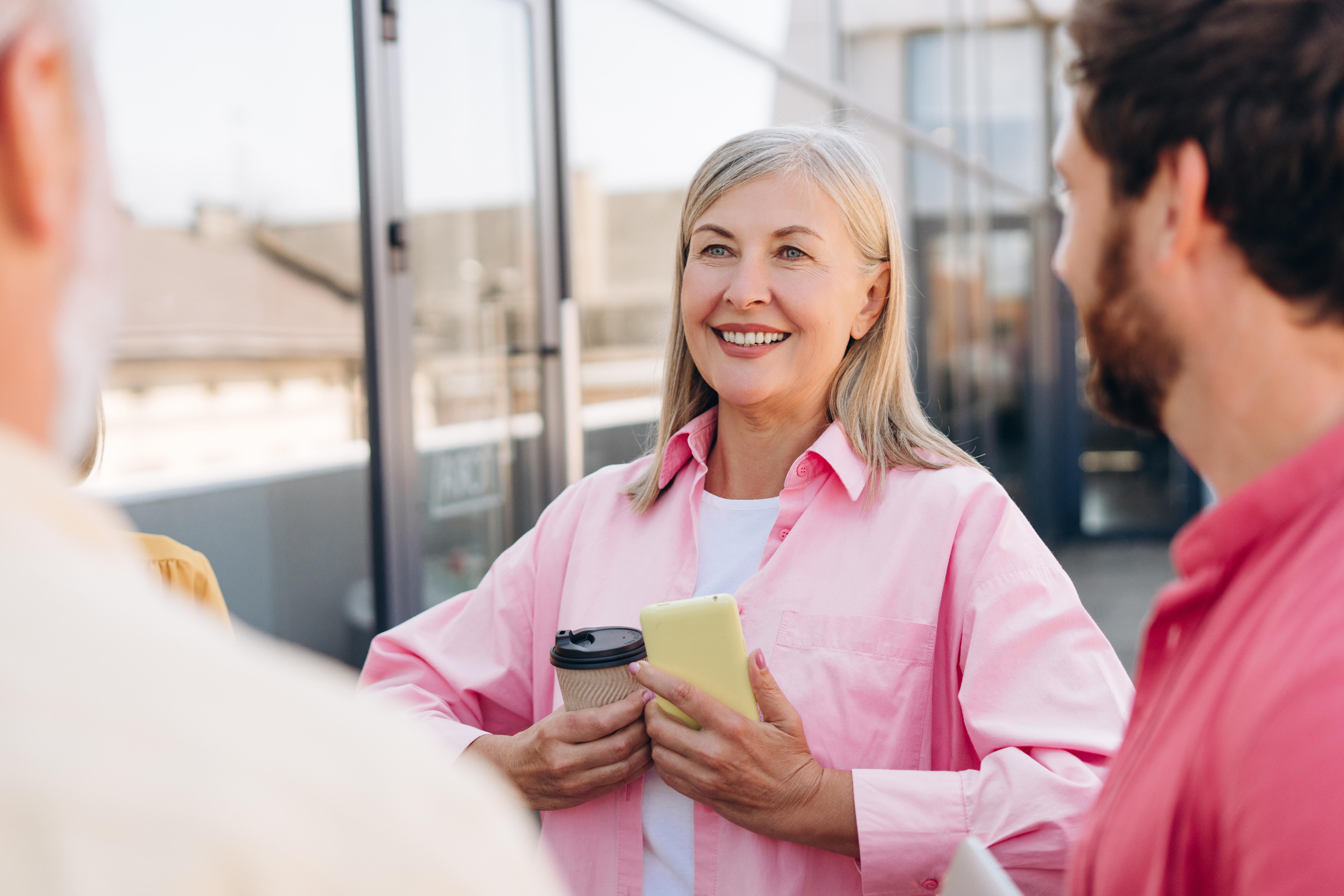 Woman with long gray hair, smiling, pink shirt, talking with two male coworkers