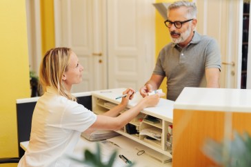 Man paying for medical bill with receptionist at desk