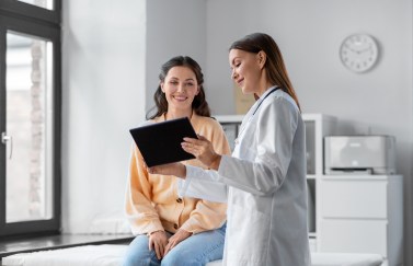Woman sitting on table, looking at tablet with doctor