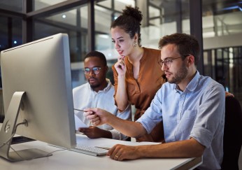 Three employees looking at computer, working, smiling