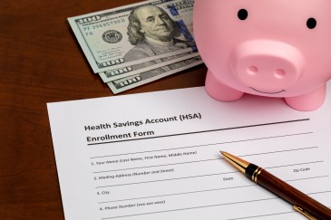Cash, a piggy bank and a health savings form are seen on a table.