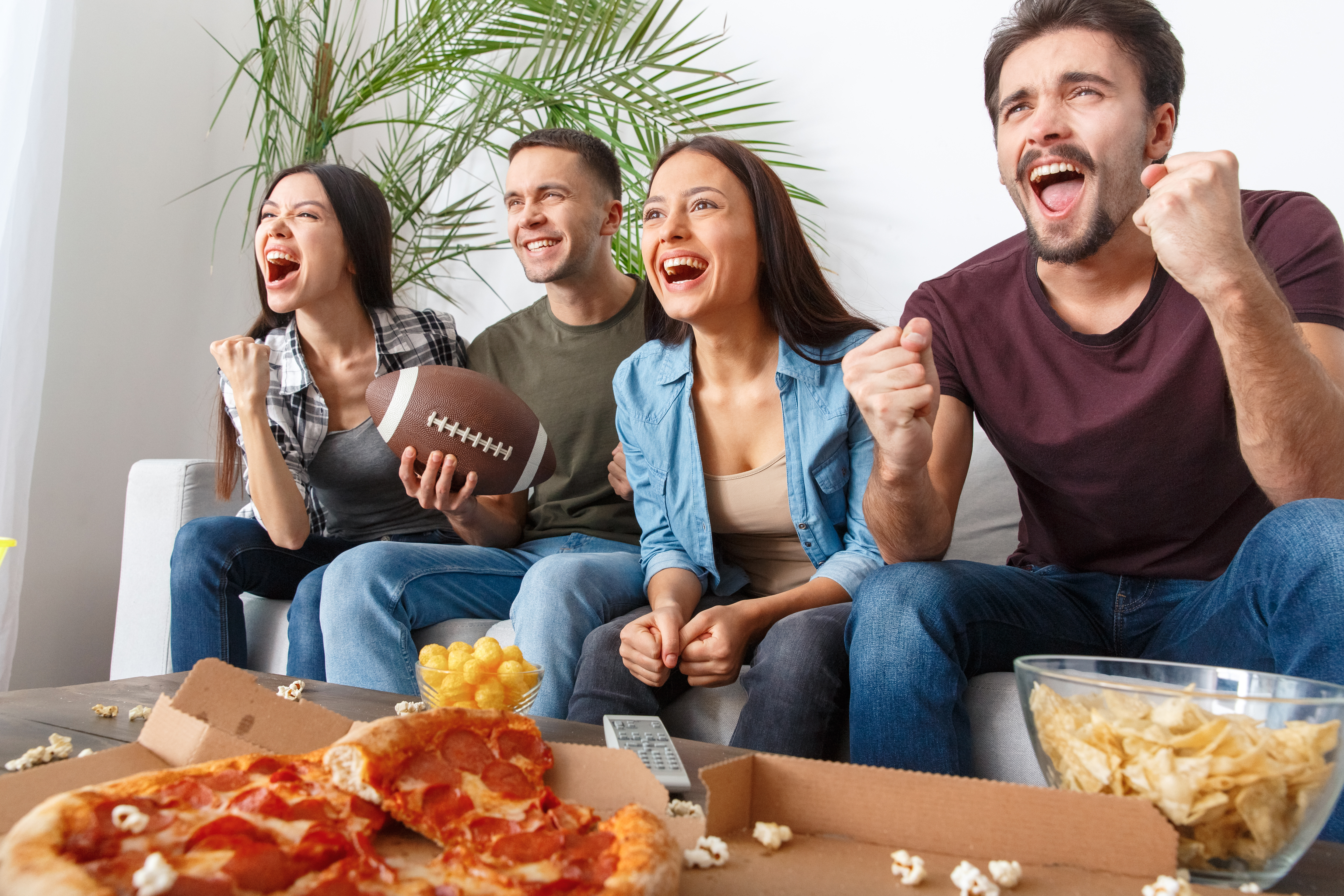 Four people sitting on couch cheering during football game