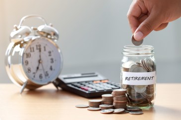 Hand putting money into jar labeled for retirement, next to clock and calculator