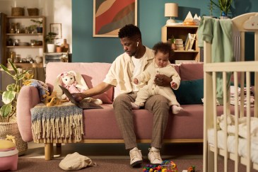 A man works at a laptop while holding a child.