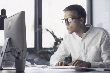 Man with glassses looking at computer screen intently