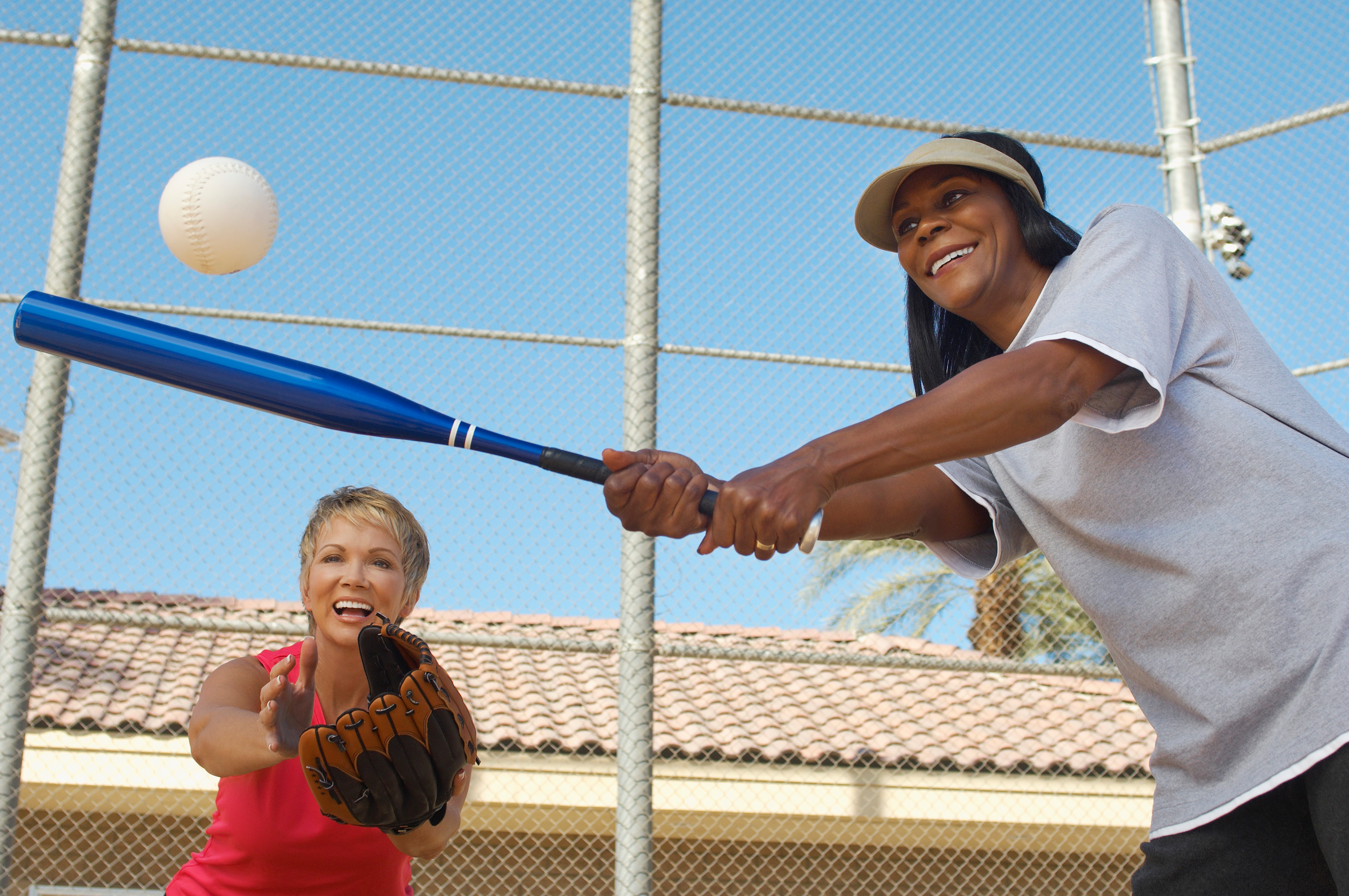 Woman hitting softball, woman behind her catching