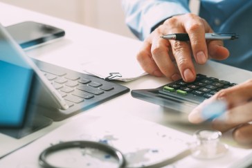 Healthcare costs and fees concept. Hand of smart doctor used a calculator for medical costs in modern hospital.