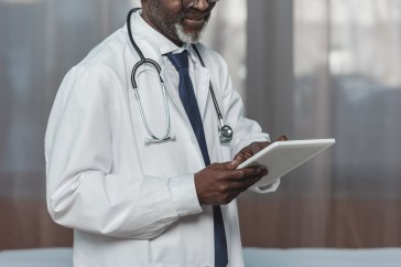 Doctor, office and tablet for research, email or communication. Medic, hospital and reading article, data or health magazine on web, while working with technology in healthcare center or clinic.
