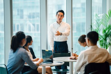 Male leader at head of conference table, speaking to four employees