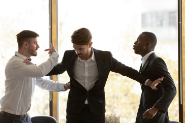 Man standing between two arguing coworkers in office; fight in office; workplace violence