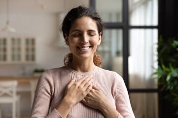 Woman smiling, eyes closed, hands resting on chest, happy