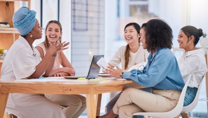 Group of women sitting at table in office working, talking