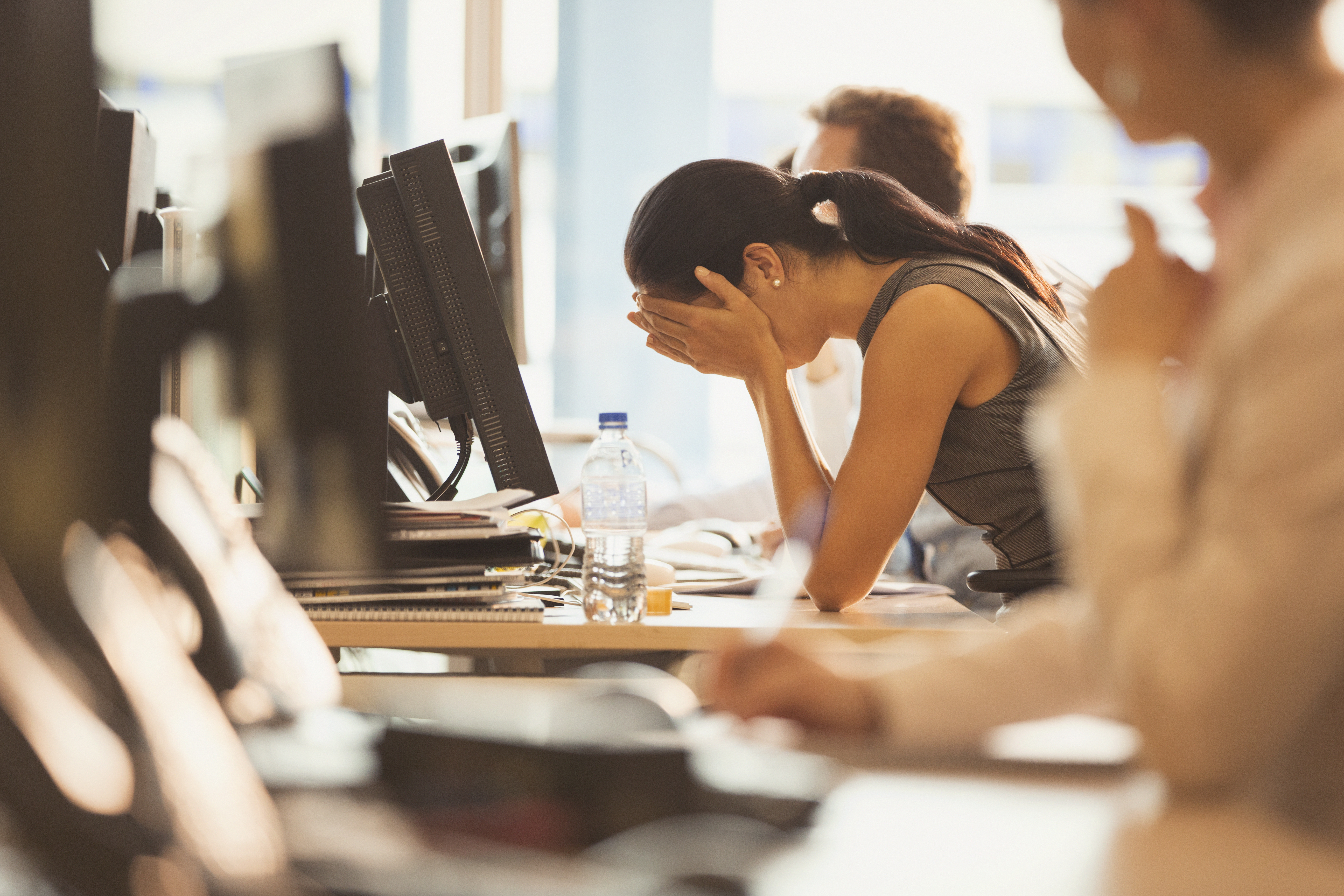 Stressed businesswoman with head in hands at office desk.