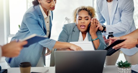 Woman on phone, sitting at desk, surrounded by people, overwhelmed, stressed